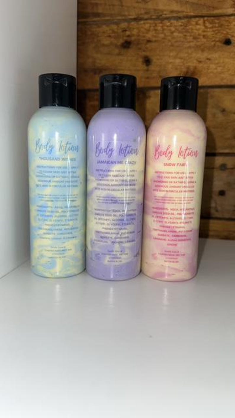 May include: Three bottles of body lotion with different scents: Thousand Wishes, Jamaican Me Crazy, and Snow Fair. The bottles are clear with a swirl of color inside. The labels are white with black text.