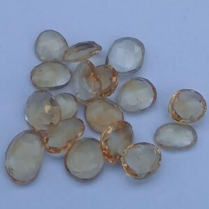 Peut inclure: Plusieurs pierres précieuses de citrine ovales et facettées. Les pierres, de tailles variées, présentent une couleur jaune doré chaleureuse. Elles sont disposées sur une surface bleu clair, mettant en valeur leur clarté.