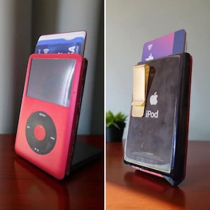 Puede incluir: Un iPod rojo modificado para guardar tarjetas de crédito. El iPod tiene una pantalla negra y un panel de control circular. La parte trasera del iPod es negra con un clip dorado y el logotipo de Apple. Se ven varias tarjetas de crédito.