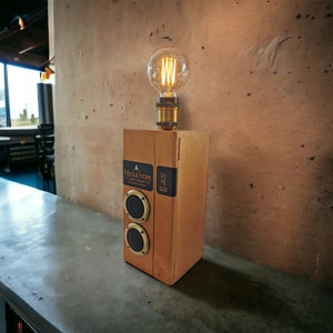 May include: A handmade wooden lamp with a vintage Edison bulb. The lamp features two circular speakers and labels from a Middleton Very Rare bottle. The lamp is on a concrete surface.