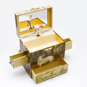 May include: A wooden music box with a unicorn design. The box has a hinged lid with a mirror inside. The unicorn spins when the music box plays. The box has a drawer on the front and two side drawers.
