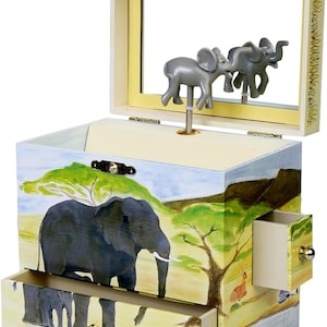 May include: A wooden music box with a safari theme. The box has a drawer and a hinged lid that opens to reveal a mirror and a spinning elephant figurine. The box is decorated with a painted scene of elephants, trees, and a watering hole.