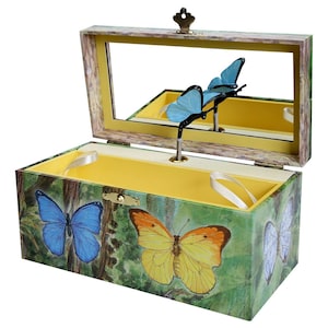 May include: A wooden music box with a butterfly design. The box is open and the lid has a mirror. The inside of the box is yellow and has a winding mechanism. The box is decorated with butterflies in shades of blue, yellow, and white.