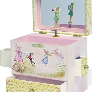 May include: A pink and yellow musical jewelry box with a fairy theme. The box features a drawer, side compartments, and a hinged lid with a mirror. Inside, a fairy figurine twirls. The exterior is decorated with fairy illustrations.