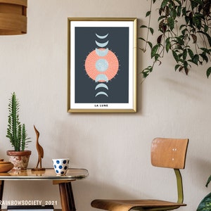 May include: A gold framed print with a dark blue background and a stylized illustration of a sun and moon phases. The text "LA LUNE" is at the bottom of the print.