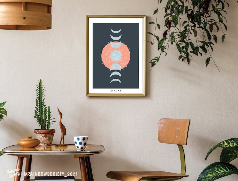 May include: A gold framed print with a dark blue background and a stylized illustration of a sun and moon phases. The text "LA LUNE" is at the bottom of the print.