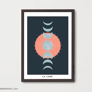May include: A framed print with a dark blue background featuring a stylized moon design with a peach-colored circle in the center and a crescent moon design in various phases. The text "LA LUNE" is at the bottom of the print.