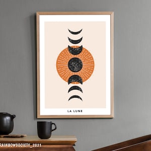 May include: A minimalist art print with a black and orange moon phase design. The print has a beige background and the text "LA LUNE" at the bottom.