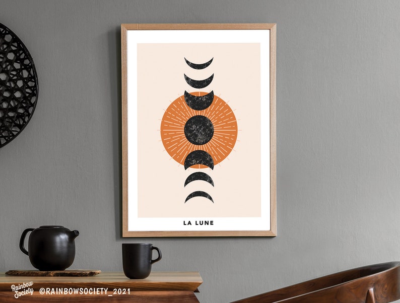 May include: A minimalist art print with a black and orange moon phase design. The print has a beige background and the text "LA LUNE" at the bottom.