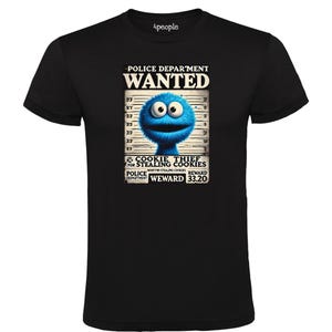 Puede incluir: Una camiseta negra con un gráfico de un personaje de monstruo de galletas azul en un cartel de se busca. El cartel dice "Police Department Wanted" y "Cookie Thief for Stealing Cookies". La recompensa se indica como "33.20".