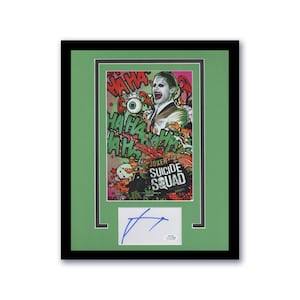 May include: Framed "Suicide Squad" movie poster featuring the Joker, with a green mat and black frame. The poster has a colorful design with the words "Joker" and "Suicide Squad". Includes a signed autograph.