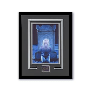 May include: A framed photograph of a woman in a black outfit, with her mouth open in a scream, kneeling in front of a tombstone. The background is a dark blue, and the image is signed in the bottom right corner.