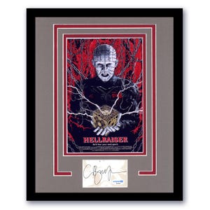 May include: Framed Hellraiser movie poster featuring Pinhead and the puzzle box, set against a red and black background. The poster includes the movie title and the tagline "He'll tear your soul apart." A signed autograph is below the poster.