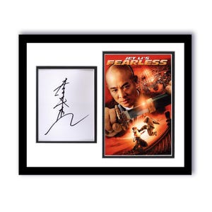 May include: Framed artwork featuring a signed autograph and a movie poster for "Jet Li's Fearless." The poster is predominantly red and features Jet Li holding a sword. The autograph is in black ink on a white background.