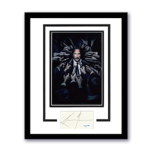 May include: Framed movie poster featuring a man in a suit surrounded by hands holding guns. The poster is in a black frame with a white mat. A signed card is below the poster.