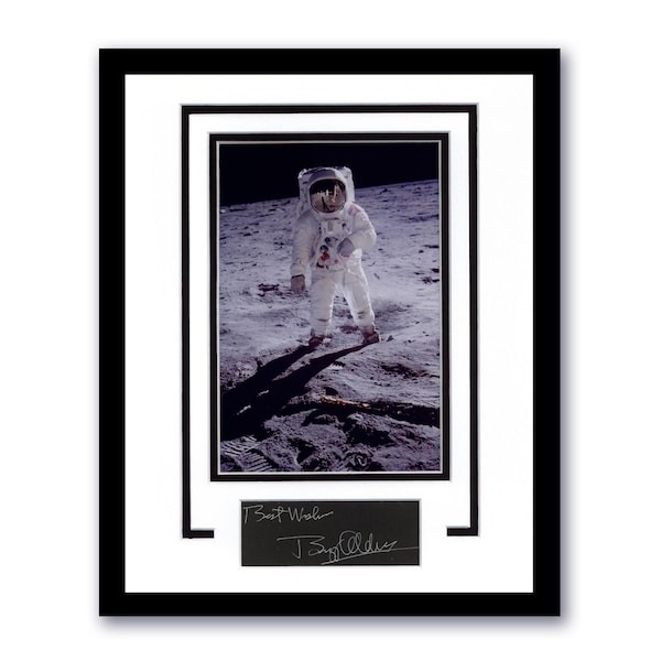 May include: Framed photograph of an astronaut on the moon, wearing a white spacesuit. The image is matted in white and framed in black. Below the photo is a black rectangle with the text "Best Wishes" and a signature.