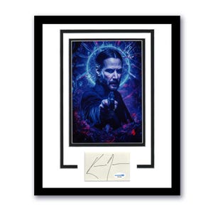 May include: Framed print of a man aiming a gun, with a blue and red background. The artwork is in a black frame with a white mount. A signed card is positioned below the print.