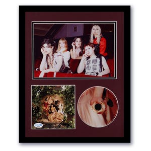 May include: A framed photo collage featuring a band of six women. The top photo shows the band members posing in a theater setting. The bottom left photo shows the band members on the cover of their album. The bottom right photo shows a close-up of a hand holding a CD.