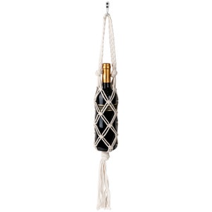 May include: A white macrame bottle holder with a tassel hanging from the bottom. A wine bottle is inside the holder.