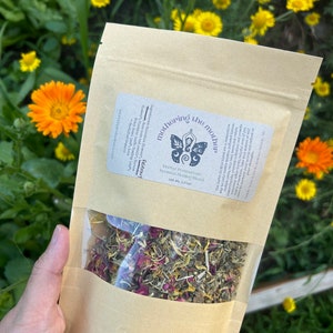 May include: A brown paper bag with a clear window showing a blend of dried herbs and flowers. The bag has a label that reads "Mothering the Mother" and "Herbal Pregnancy Blend".
