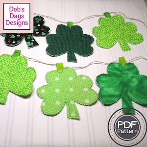 May include: A string of green shamrock fabric cutouts, each with a different pattern, hanging from a twine string. The shamrocks are decorated with polka dots, small flowers, and a tie-dye pattern. The text "PDF Pattern" is visible in a circle at the bottom of the image.