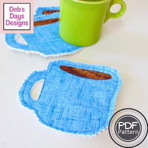 May include: Blue fabric coffee cup coasters with a brown coffee cup design. The coasters have a scalloped edge and a hole for a handle. The text "PDF Pattern" is on a white circle with a black border.