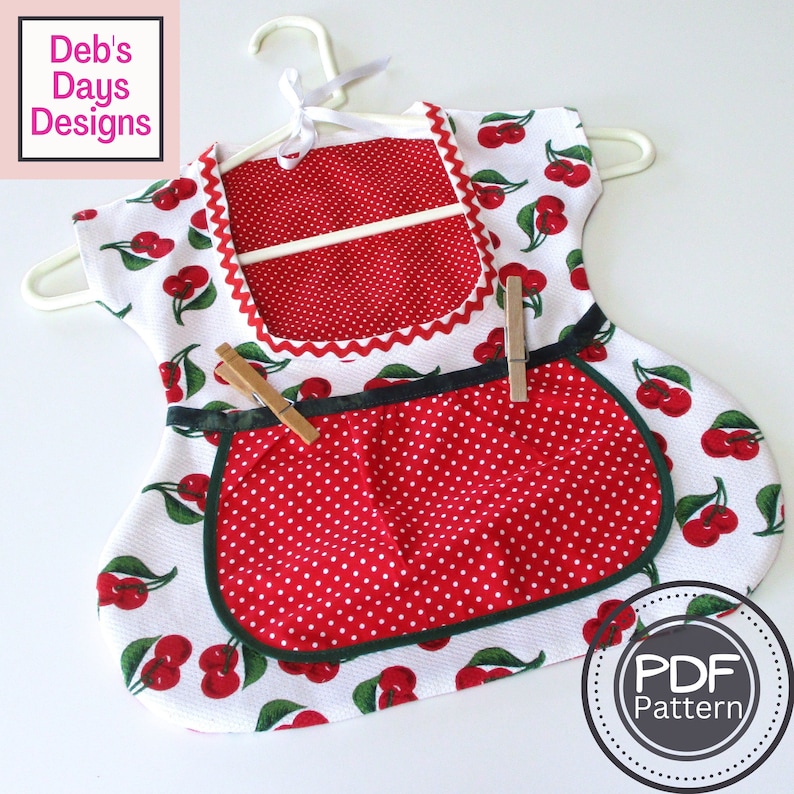 May include: A red and white cherry print apron with a polka dot pocket and a green trim. The apron has a hanger and two wooden clothespins attached to it. The text "PDF Pattern" is visible in the lower right corner of the image.