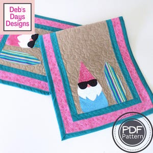 Può includere: Due tovagliette trapuntate con un design a gnomo. Gli gnomi indossano occhiali da sole e cappelli rosa. Le tovagliette hanno uno sfondo beige, bordi turchese e finiture rosa fantasia. Il testo "Deb's Days Designs" e "PDF Pattern" sono visibili.