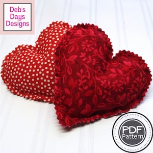 May include: Two red fabric heart-shaped pillows. One pillow has a white polka dot pattern and the other has a red floral pattern. The pillows are on a white surface. The text "PDF Pattern" is in a circle on the bottom right of the image.