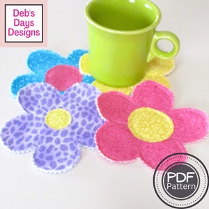 May include: Four colorful flower-shaped fabric coasters with a green mug sitting on top of one of the coasters. The coasters are made of different patterned fabrics and have a white border. The text "PDF Pattern" is visible in the lower right corner of the image.