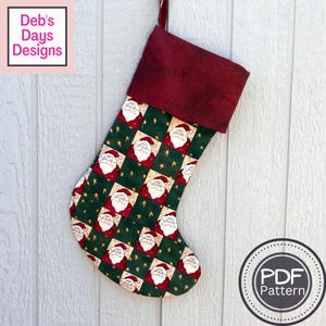 May include: A red and green Christmas stocking with a Santa Claus pattern. The stocking has a red felt cuff and is hanging on a white wooden wall. The text "PDF Pattern" is visible in a circle on the bottom right corner of the image.