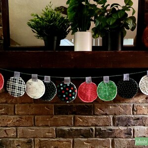 Puede incluir: Una guirnalda navide&ntilde;a hecha de c&iacute;rculos de tela con varios patrones navide&ntilde;os, incluyendo copos de nieve, renos y cuadros. La guirnalda est&aacute; enhebrada con una cinta gris y colgada sobre una chimenea de ladrillo.