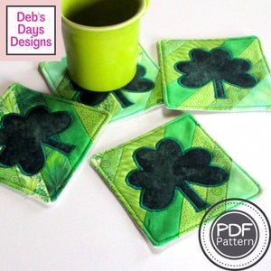 May include: Four square, quilted coasters with a shamrock design. The coasters are primarily green with a dark green shamrock applique. A green mug sits on one coaster. The image includes the text "Deb's Days Designs" and "PDF Pattern".