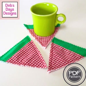 Könnte beinhalten: Drei dreieckige Stoffuntersetzer mit einem rot-weißen Karomuster und einem grünen Rand. Eine grüne Tasse steht auf einem der Untersetzer. Die Untersetzer sind mit "PDF-Muster" beschriftet.