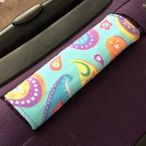 May include: A turquoise luggage handle cover with a paisley pattern in shades of purple, orange, yellow, and white.
