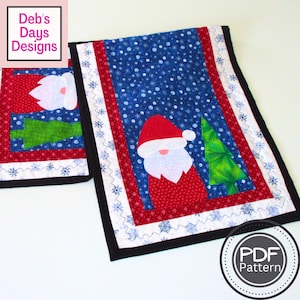 May include: Christmas-themed quilted table runner and matching placemat. The runner features a Santa Claus design with a red hat and beard, a green Christmas tree, and a blue snowflake background. The placemat has a similar design. The edges are black.