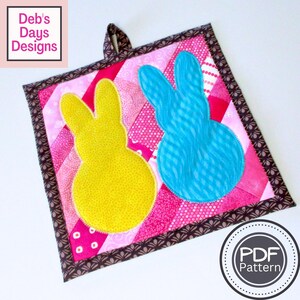 May include: A pink and brown patchwork hot pad with a blue and yellow bunny applique. The hot pad has a brown loop for hanging. The text "PDF Pattern" is on a white circle in the lower right corner.