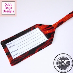 以下が含まれることがあります： 鮮やかな赤と黒の抽象的な模様のラゲッジタグ。名前、住所、電話番号、メールアドレス用の白い長方形のセクションがあります。タグはストラップに取り付けられています。「Deb's Days Designs」の文字が左上にあります。