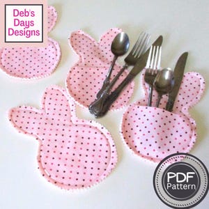 May include: Four pink and brown polka dot bunny-shaped fabric place card holders with silver cutlery inside. The text "PDF Pattern" is on a white circle with a black border.