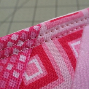 Puede incluir: Primer plano de una tela rosa y roja con un patr&oacute;n geom&eacute;trico. La tela est&aacute; cosida con una puntada recta a lo largo del borde.