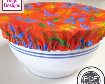 May include: A red fabric bowl cover with a floral pattern in shades of blue, yellow, and green. The cover is on top of a white bowl with blue stripes. The text "PDF Pattern" is on a white circle with a black border.