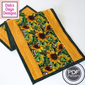 Könnte beinhalten: Gesteppter Tischläufer mit einem Sonnenblumen- und Vogelmuster auf schwarzem Hintergrund, umrahmt von einem gelben Rand und dunkelgrünen Zierleisten. Der Text "Deb's Days Designs" befindet sich in der oberen linken Ecke. Das PDF-Muster ist verfügbar.