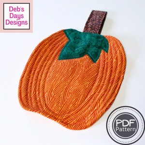 May include: A quilted pumpkin-shaped hot pad with a green fabric stem and a brown fabric loop handle. The hot pad is made of orange and yellow fabric with a striped pattern. The text "PDF Pattern" is printed on a white circle with a black border.
