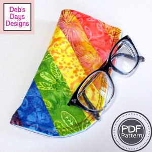 May include: A rainbow striped fabric eyeglass case with a pair of glasses on top. The case is made of a soft, colorful fabric with a floral pattern. The glasses are black with clear lenses. The text "PDF Pattern" is visible in a circle on the right side of the image.
