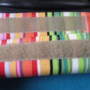 May include: Two colorful striped fabric luggage straps with velcro closures. The straps are attached to a blue suitcase.