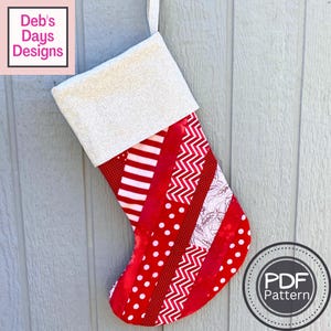 May include: A red and white patchwork Christmas stocking with a white cuff. The stocking is made of various red and white fabrics, including stripes, polka dots, and zigzags. The cuff is made of a white fabric with a subtle pattern. The stocking is hanging on a gray wooden wall. The text "PDF Pattern" is visible in the lower right corner of the image.