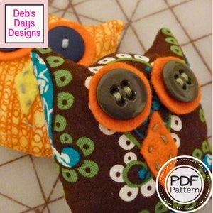 May include: Two brown and orange fabric owls with button eyes. The owls are sitting on a patterned surface. The text "PDF Pattern" is in a circle on the bottom right of the image.