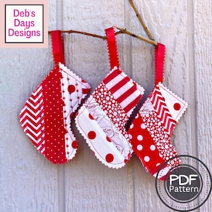 Pode incluir: Três meias de Natal de tecido patchwork vermelho e branco penduradas em um galho. As meias são feitas de diferentes tecidos estampados vermelhos e brancos, incluindo bolinhas, listras e ziguezagues. O texto "PDF Pattern" é visível no canto inferior direito da imagem.