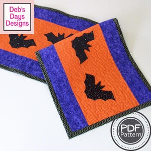 Peut inclure: Chemin de table matelassé sur le thème d'Halloween avec des panneaux orange et violets. Des appliqués de chauve-souris noires sont présents sur les panneaux centraux orange. Les bords sont bordés d'un motif en zigzag noir et vert.