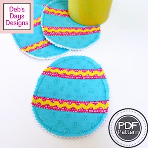 Puede incluir: Cuatro posavasos azules y blancos en forma de huevo con rayas rosas y amarillas. Los posavasos están hechos de tela y tienen un borde festoneado. El texto "PDF Pattern" es visible en la esquina inferior derecha de la imagen.
